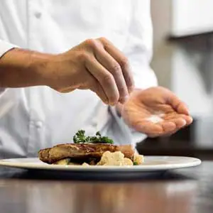 Chef seasoning a dish in a professional kitchen, highlighting Boulder Salt as a low-sodium alternative for culinary excellence.